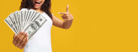 Loan, credit concept. African american woman holding bunch of money over yellow studio background, panorama, empty spaceの写真素材