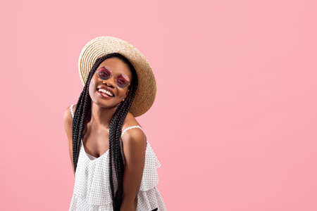 Playful black woman with afro bunches looking at camera and smiling, advertising trendy summer outfit on pink backgroundの写真素材