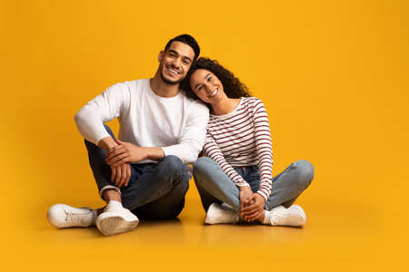 Romantic young middle eastern couple sitting on floor over yellow backgroundの写真素材