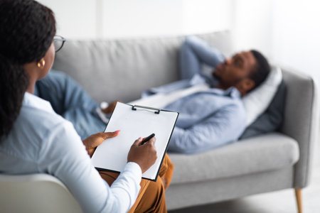 Psychologist working with black male patient at office, mockup for design on clipboardの写真素材
