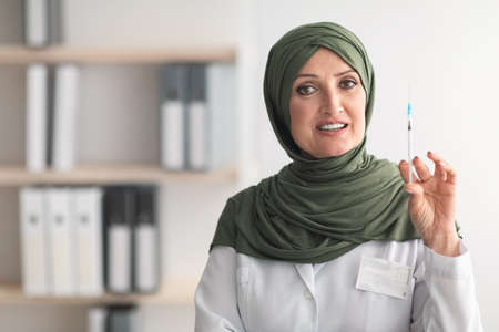 Mature Muslim Doctor Lady Holding Syringe Standing In Clinicの写真素材
