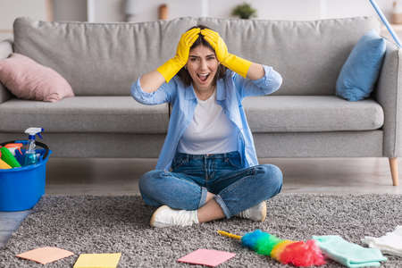 Screaming woman tired of cleaning sitting on floor carpetの写真素材