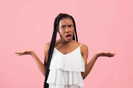 Irritated African American woman showing I DONT KNOW gesture, shrugging shoulders on pink studio backgroundの写真素材