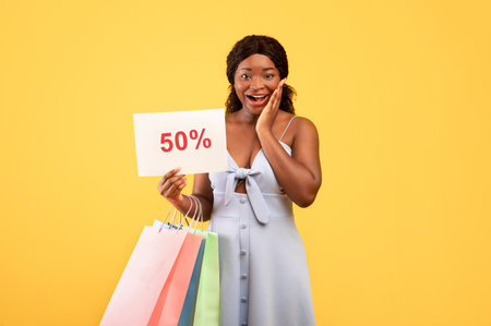 Huge summer sales. Excited young African American woman holding shopping bags and FIFTY PERCENT OFF...