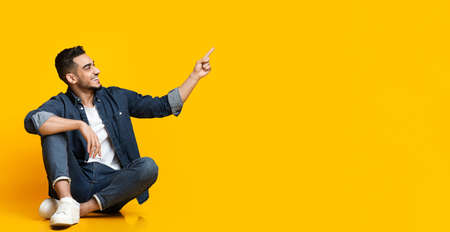 Handsome arab guy sitting on floor, pointing at copy spaceの写真素材