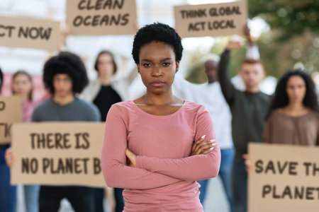 Serious young black lady standing over crowd with placardsの写真素材