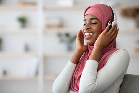 Domestic Leisure. Relaxed Black Muslim Lady In Hijab Listening Music In Headphonesの写真素材