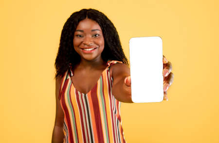 Black woman showing cellphone with blank screen to camera over orange background, mockup for mobile app or websiteの写真素材