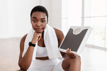 Portrait of Unhappy African Woman Holding Bathroom Scales. Slimmingの写真素材