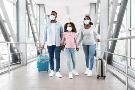 Black family in masks traveling, walking in modern airportの写真素材