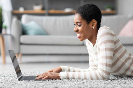 Side View Of Cheerful Black Woman Using Laptop Computer At Homeの写真素材