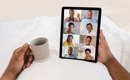 Black male videochatting with friends while relaxing with digital tablet in bedの写真素材