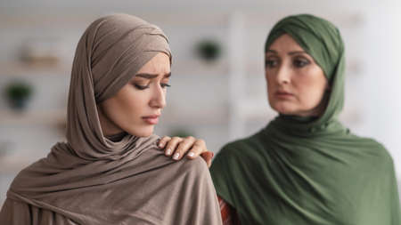 Senior Muslim Mother Supporting Unhappy Adult Daughter Standing At Home