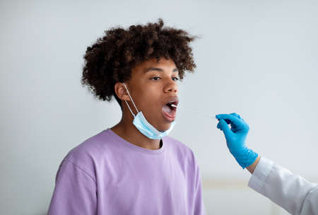Doctor making oral  PCR test for black teenage patient at clinic. Infectious disease prevention conceptの写真素材