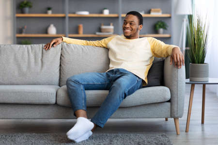 Joyful african american guy sitting on sofa at home