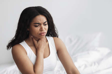 Healthcare concept. Sad sick african american woman coughing, suffering from sore throat, sitting in...