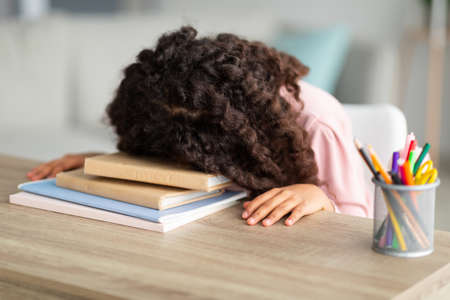 Overworked african american schoolgirl resting head on desk, tired of homework, sitting at home in living room interiorの写真素材