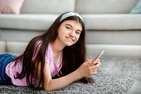 Indian adolescent girl with mobile phone studying online, chatting with friend, browsing social media at homeの写真素材