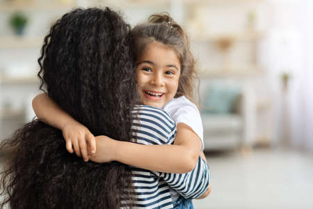 Cute little girl hugging her mother and cheerfully smilingの写真素材