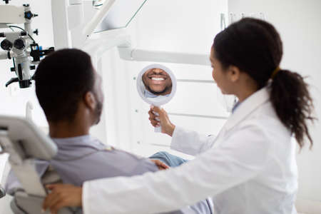 Black Guy Looking At Mirror, Checking His Teeth After Dental Treatmentの写真素材