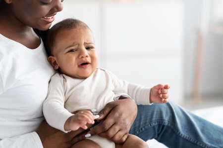 Black lady holding crying baby with colic on handsの写真素材