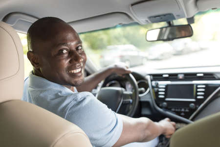 Cheerful black guy driver sitting inside brand new car