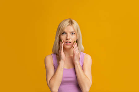 Oh no. Shocked young lady looking at camera and covering mouth with hands, standing isolated over...