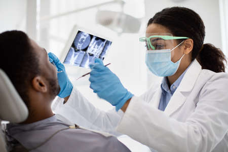 Black Dentist Lady Examining Teeth Of Male Patient With Sterile Dental Toolsの写真素材