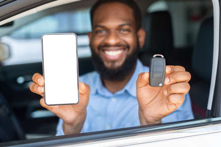 Car Renting App. Black Man Showing Key And Smartphone With Blank Screenの写真素材