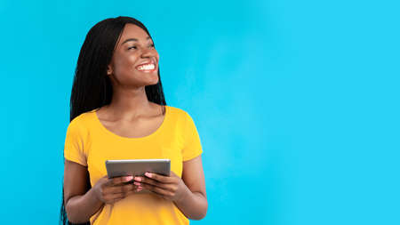 Black woman using digital tablet looking aside over blue background