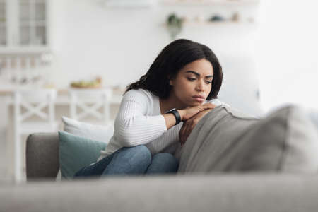Depressed african american woman sitting on sofa, spending weekend on her own, feeling lonely, copy spaceの写真素材