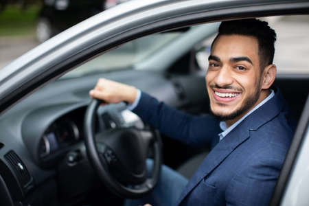 Happy handsome middle-eastern businessman driving car to airport, side viewの写真素材