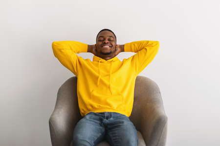 Black Guy Sitting With Hands Behind Head In Armchair Indoorの写真素材