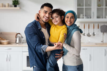 Happy Middle-Eastern Father, Mother And Little Daughter Posing Together In Kitchen Interiorの写真素材