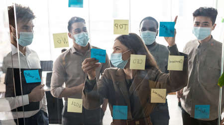 Business people in disposable masks brainstorming using notes on wall