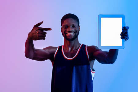 Positive black sportsman showing tablet pc with empty screen in neon light, mockup for app or...