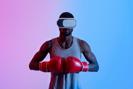 Strong black sportsman in VR headset putting boxing gloves together in neon lightの写真素材