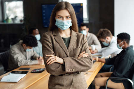 Young business lady in mask sitting on desk and posingの写真素材