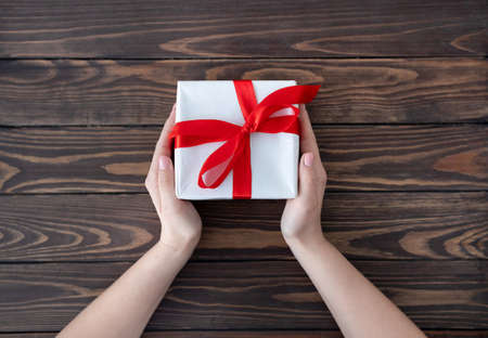 Woman giving wrapped christmas or other holiday handmade present in white paper with red ribbon, wooden table, top viewの写真素材