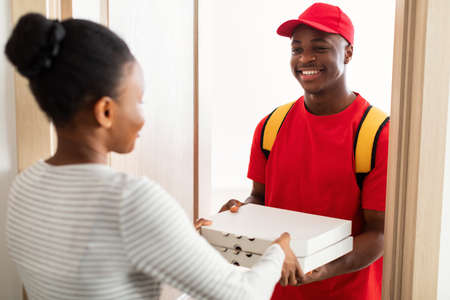 Cheerful Black Courier Standing Holding Pizza Boxes At Customers Doorsの写真素材