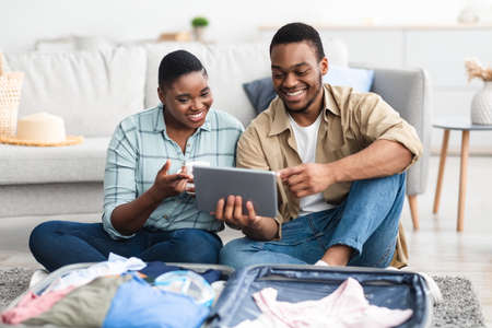 Happy Black Travelers Couple Using Digital Tablet At Homeの写真素材