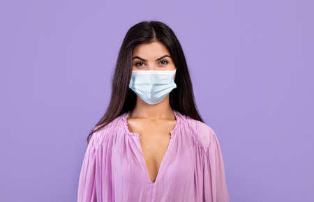 Virus protection concept. Portrait of armenian woman in protective medical mask on face over purple backgroundの写真素材
