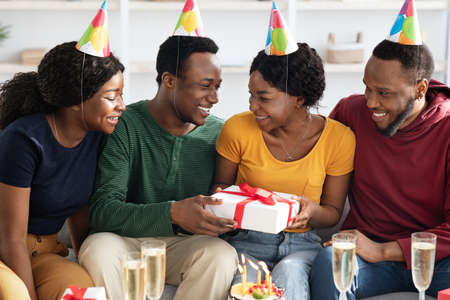 Joyful black friends greeting birthday guy at homeの写真素材