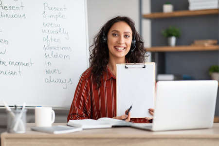 Female teacher in headphones sitting at desk shower paper document