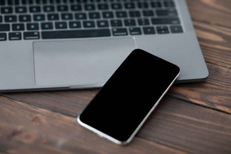 Modern smartphone with black blank screen placed near laptop computer, closeup. Mockup for your design or advertisementの写真素材