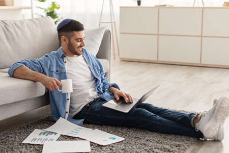 Man working on laptop at home on floor drinking coffee