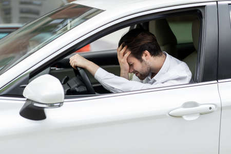 Businessman sitting in own car stuck in traffic, holding his hand on forehead and nervously waiting