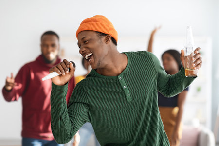 Joyful african american man with bottle of beer singing karaokeの写真素材