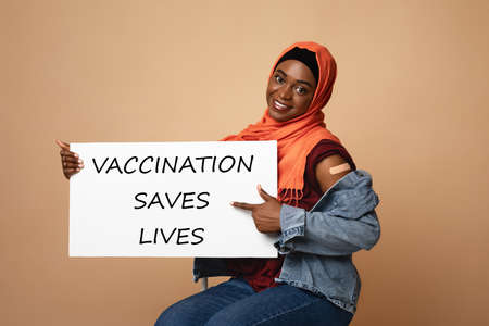 Happy muslim woman with plaster on shoulder holding placardの写真素材