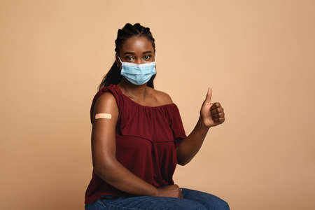 Vaccinated black woman recommending immunization, showing thumb up
